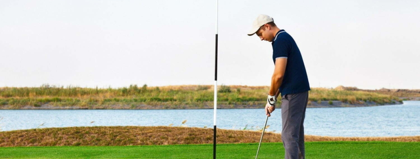 Athletic young man playing golf in golf club near the water